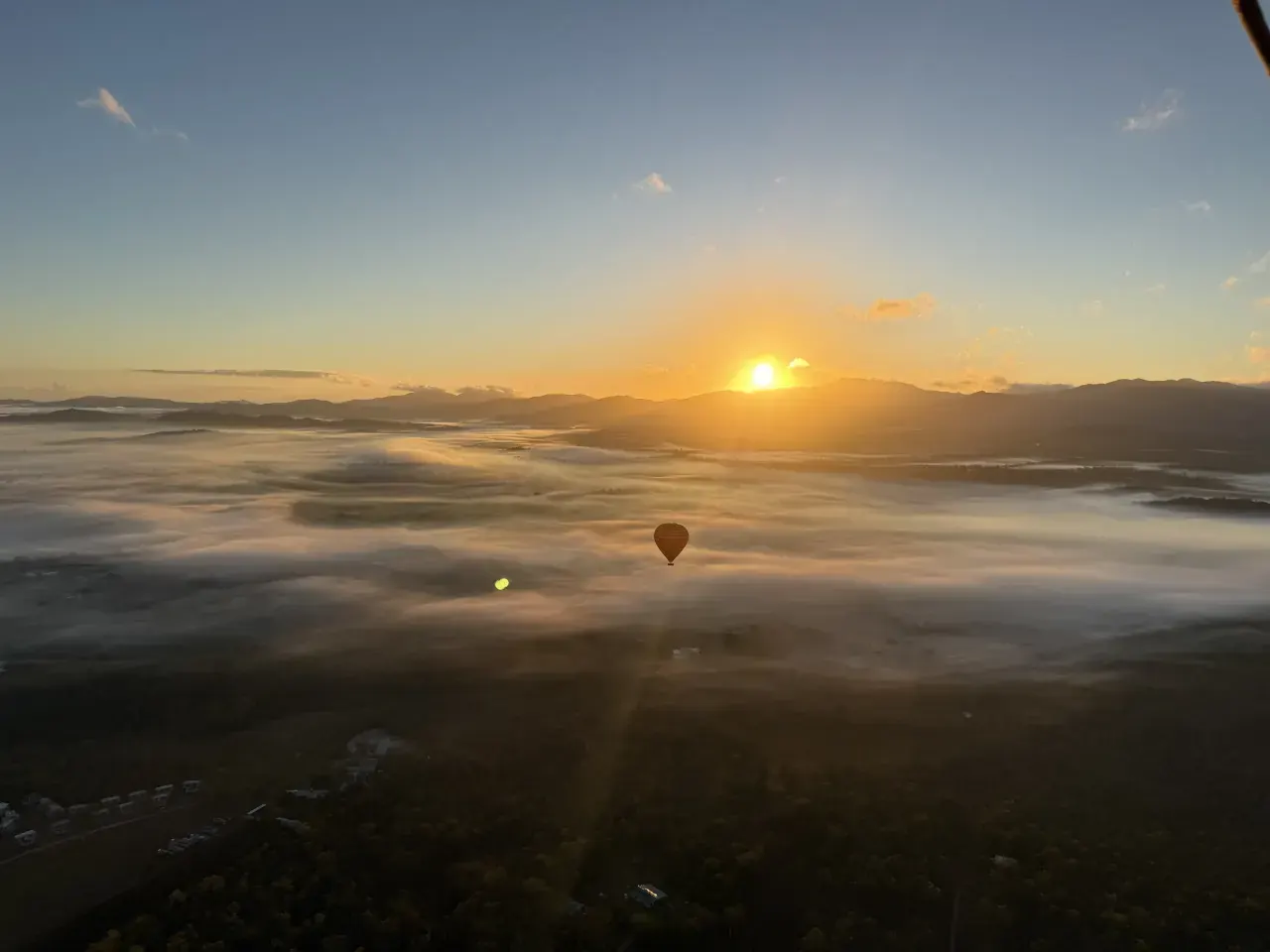 Sunrise above misty fields with another hot-air balloon below