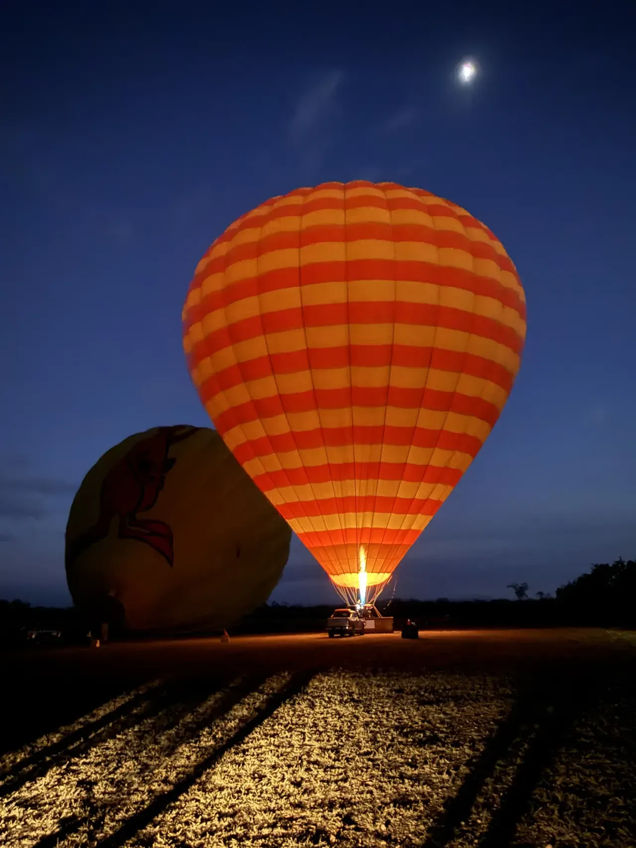 A hot-air balloon inflating beneath the Moon before dawn