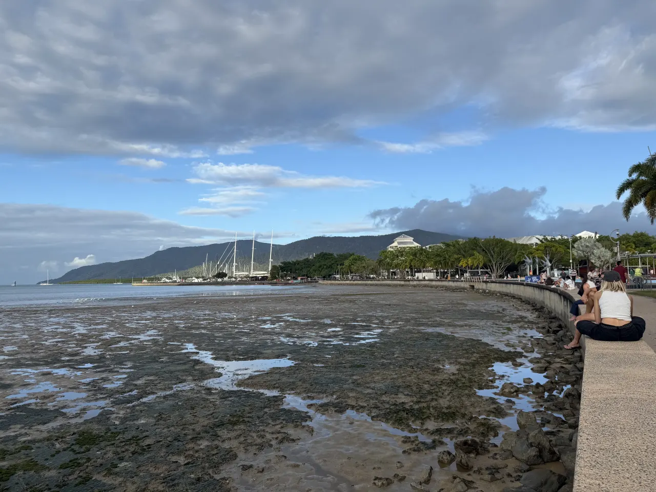 People sitting on the seawall above the low-tide bay