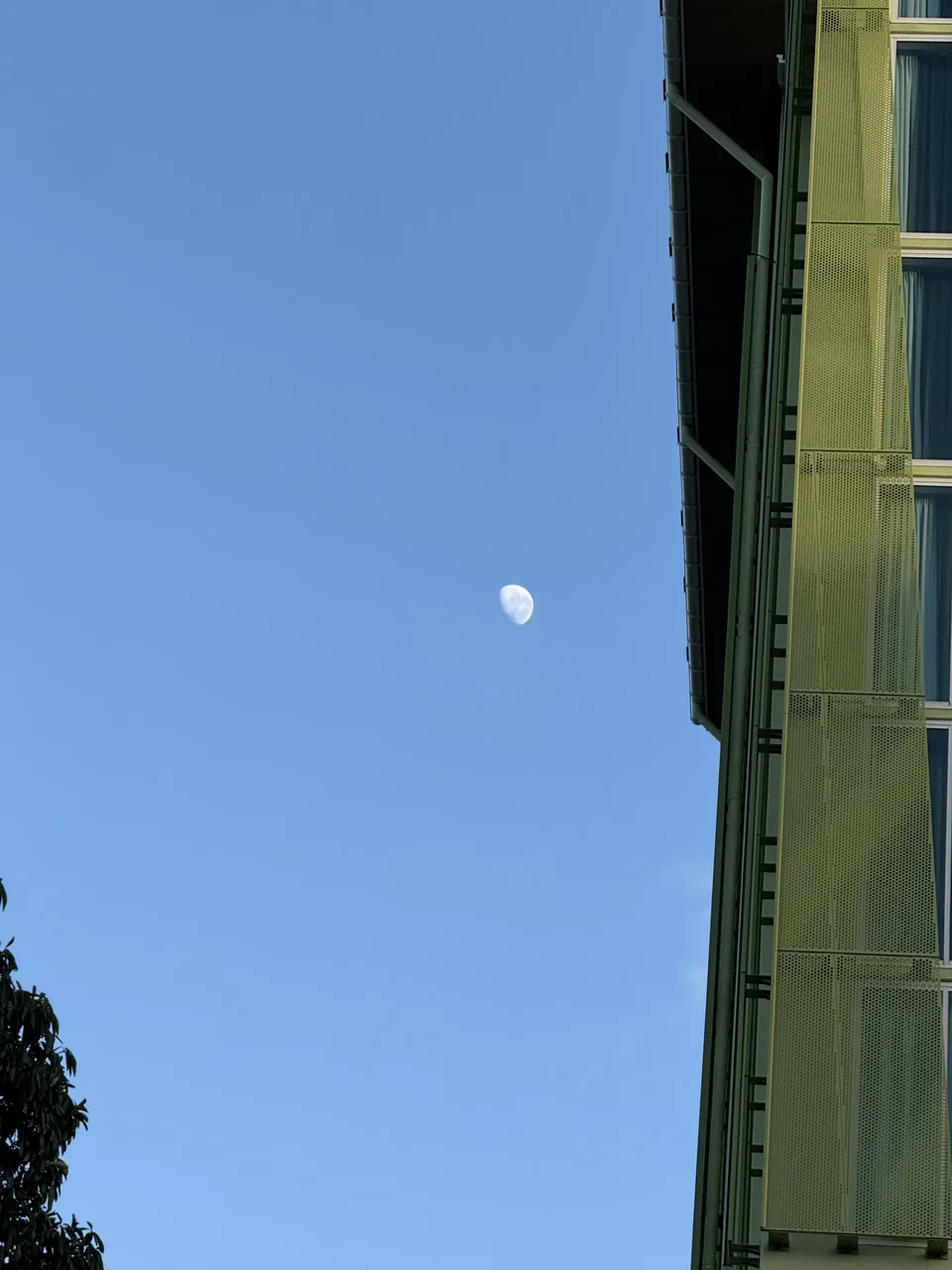 The daytime Moon in a blue sky beside the hotel