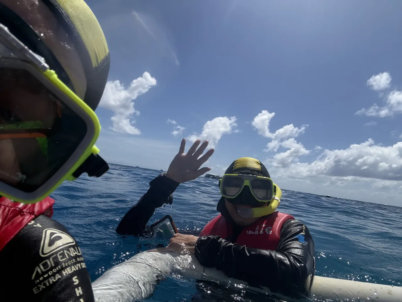 Two snorkelers in yellow masks and red flotation vests, one waving